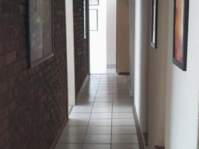 A functional hallway featuring a textured exposed brick wall and neutral ceramic floor tiles, providing a clean transition between living spaces.