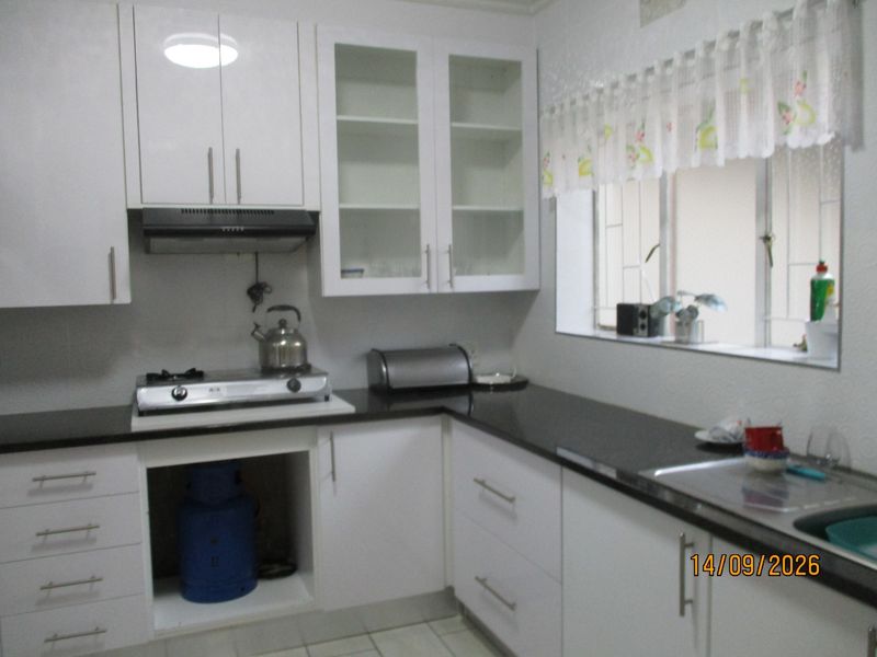 A functional kitchen featuring white cabinetry, dark granite countertops, a gas hob with extractor fan, and a stainless steel sink.