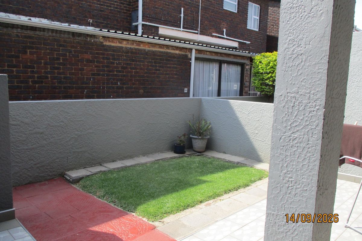 A private rear courtyard featuring a small lawn area, paved patio space, and enclosed boundary walls.
