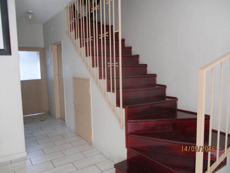 Entrance area featuring a wooden staircase with metal balustrade, tiled flooring, and under-stair storage access.