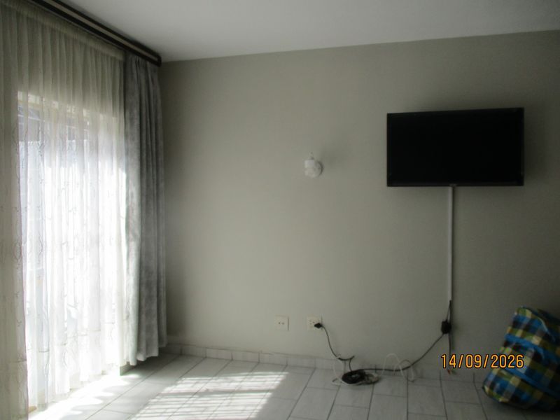 A simple living area featuring tiled flooring, a sliding glass door with curtains, and wall-mounted electrical and lighting fixtures.