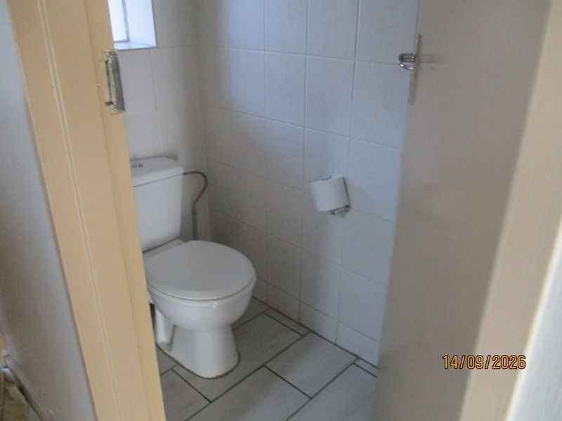 A compact guest bathroom featuring white ceramic wall tiles, tiled flooring, and a standard toilet suite.