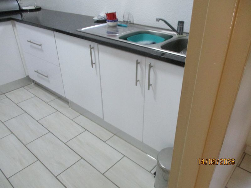 A functional kitchen area featuring white cabinetry, dark stone countertops, a stainless steel sink, and light-colored tiled flooring.