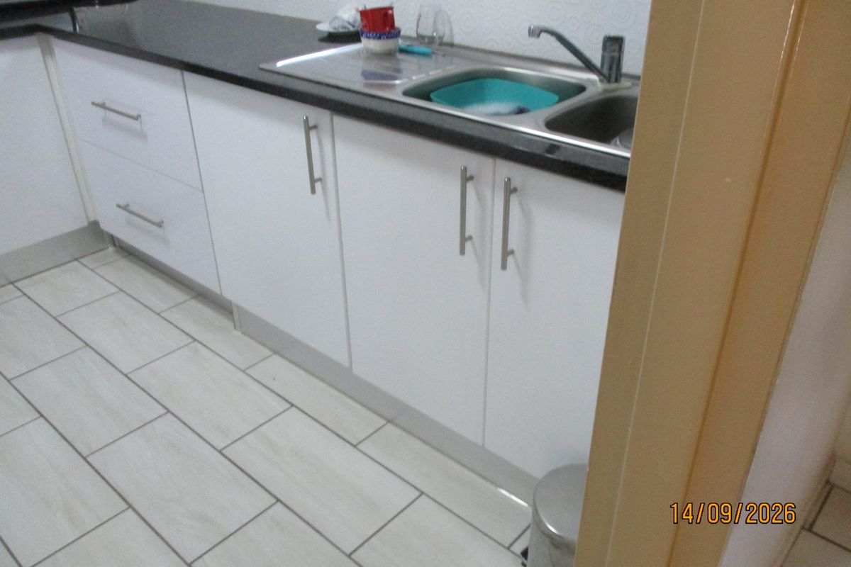 A functional kitchen area featuring white cabinetry, dark stone countertops, a stainless steel sink, and light-colored tiled flooring.