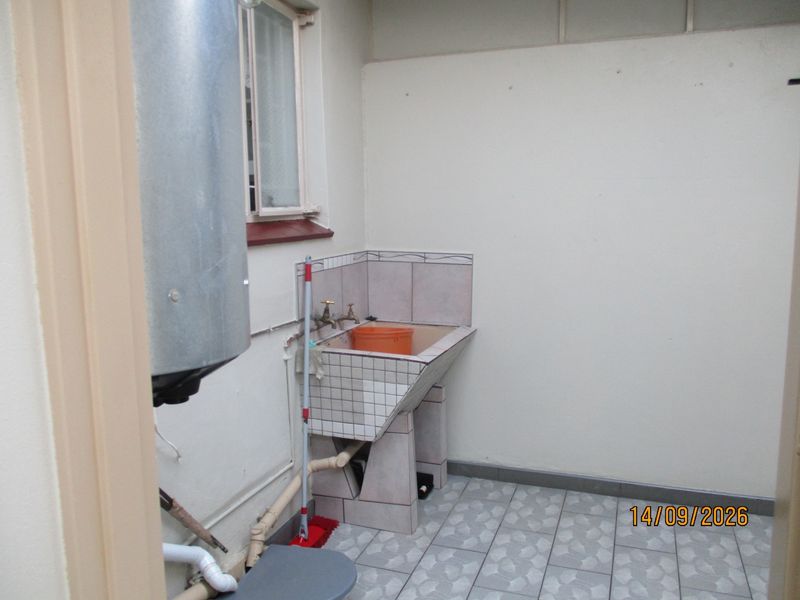 A functional laundry area featuring a tiled utility sink, exposed plumbing, and an electric water heater.