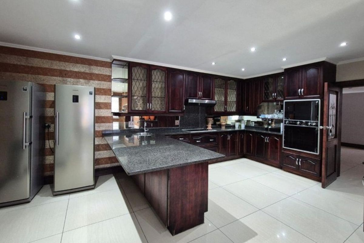 Spacious kitchen featuring dark wood cabinetry, granite countertops, built-in oven, extractor fan, and modern tiled flooring with recessed lighting.