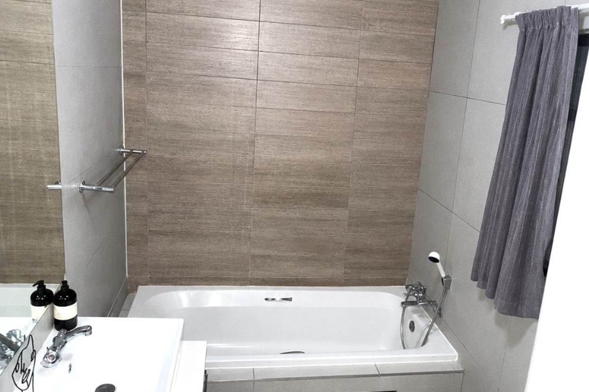 Modern bathroom featuring a built-in bathtub with tiled surround, vanity basin with storage cabinet, and neutral wall and floor tiling.