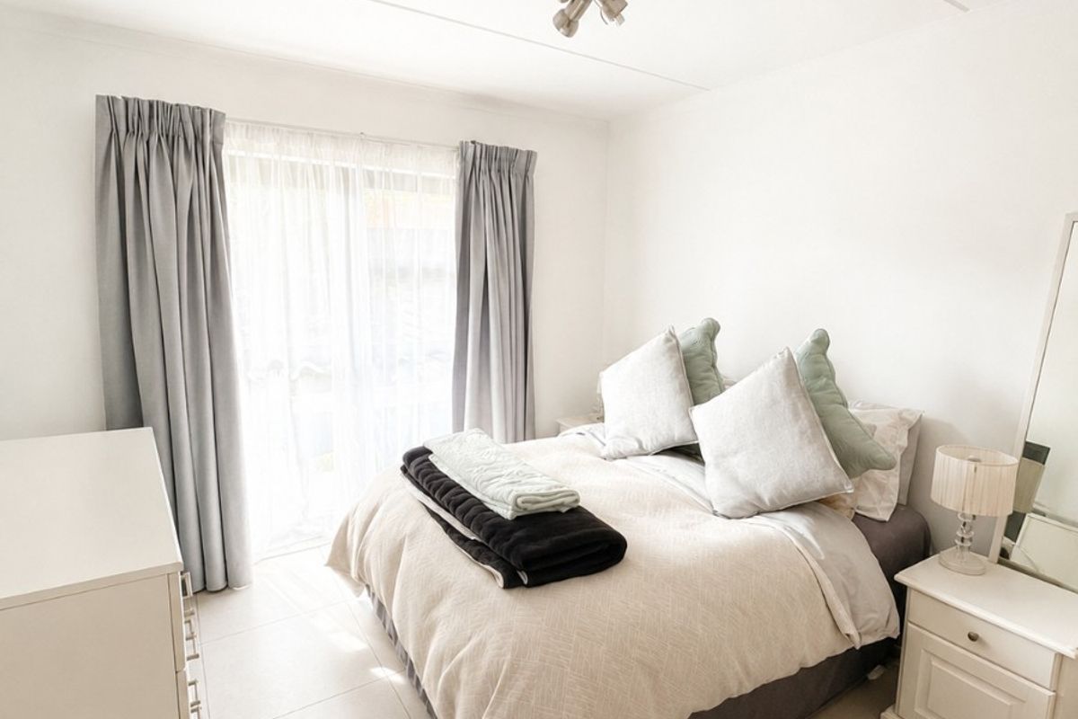 A bright and well-maintained bedroom featuring neutral tiled flooring, a modern ceiling spotlight, and a sliding glass door providing access to the exterior.
