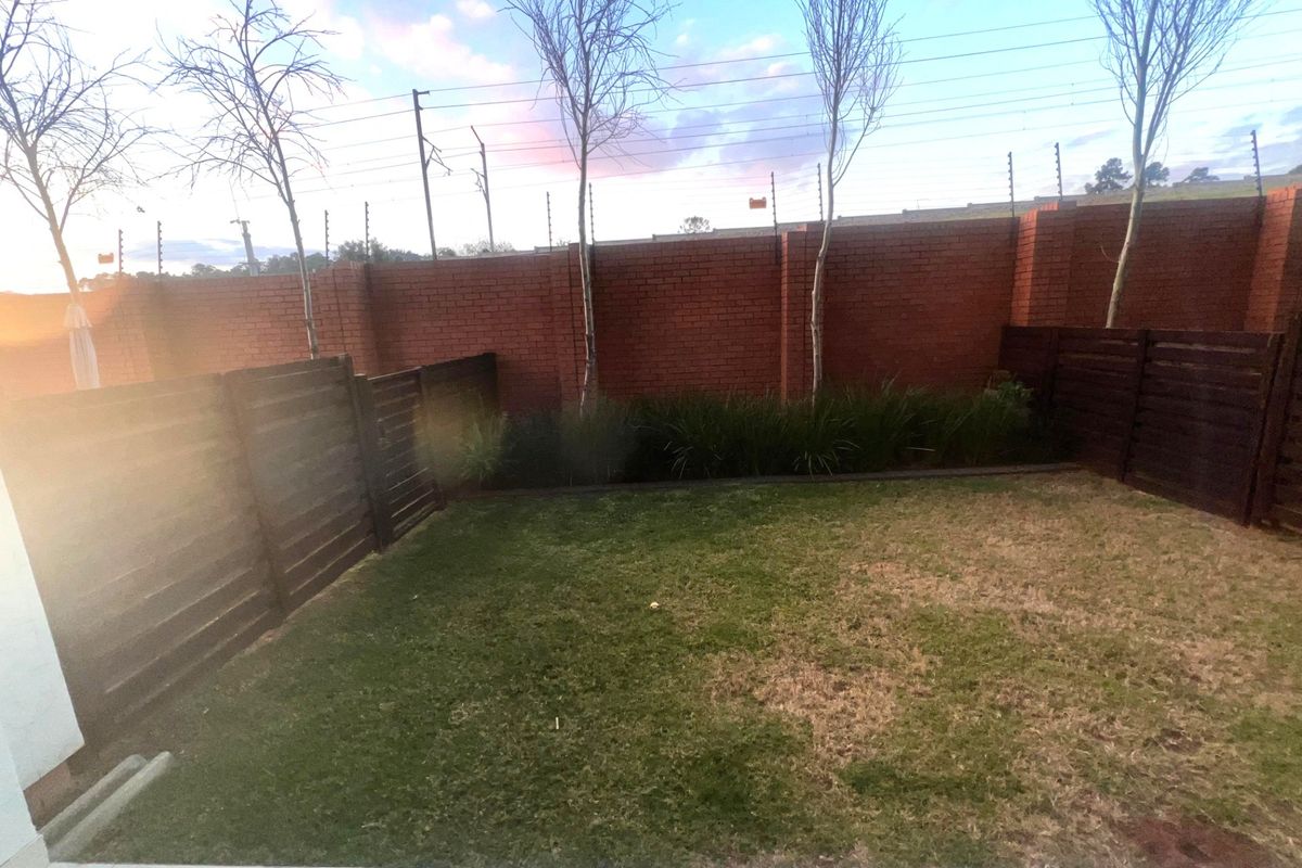 A private rear garden featuring a tiled patio, lawn area, and secure brick boundary walls with integrated electric fencing.