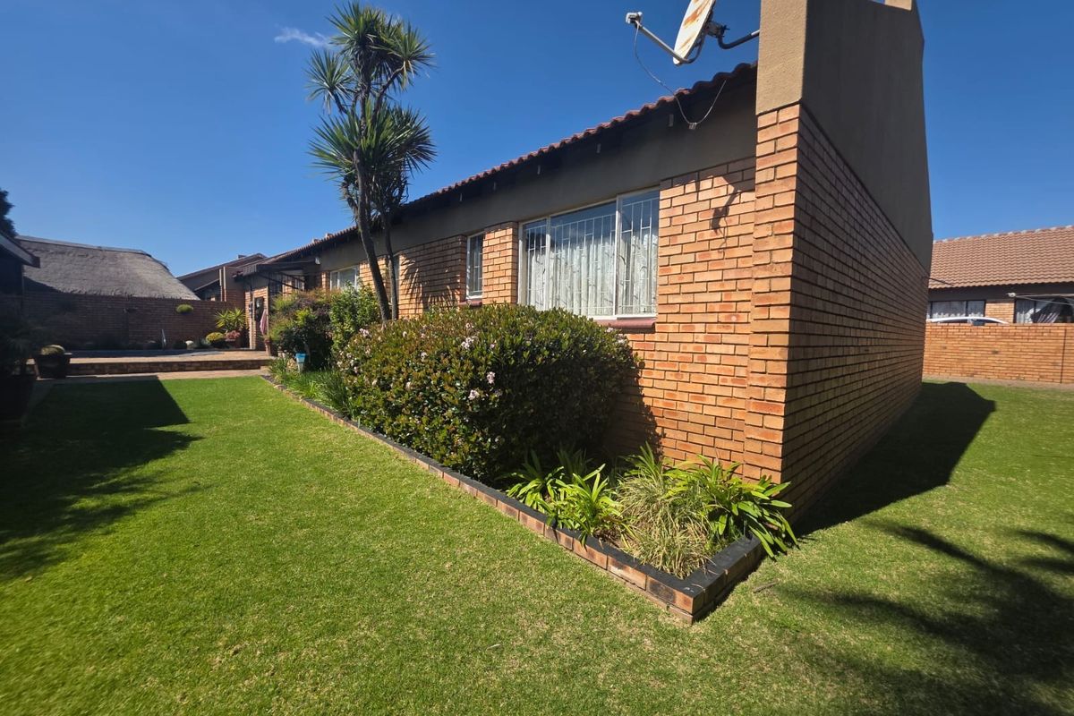 A well-maintained rear exterior view of the house featuring a brick facade, tiled roof, and a neat, landscaped garden area.