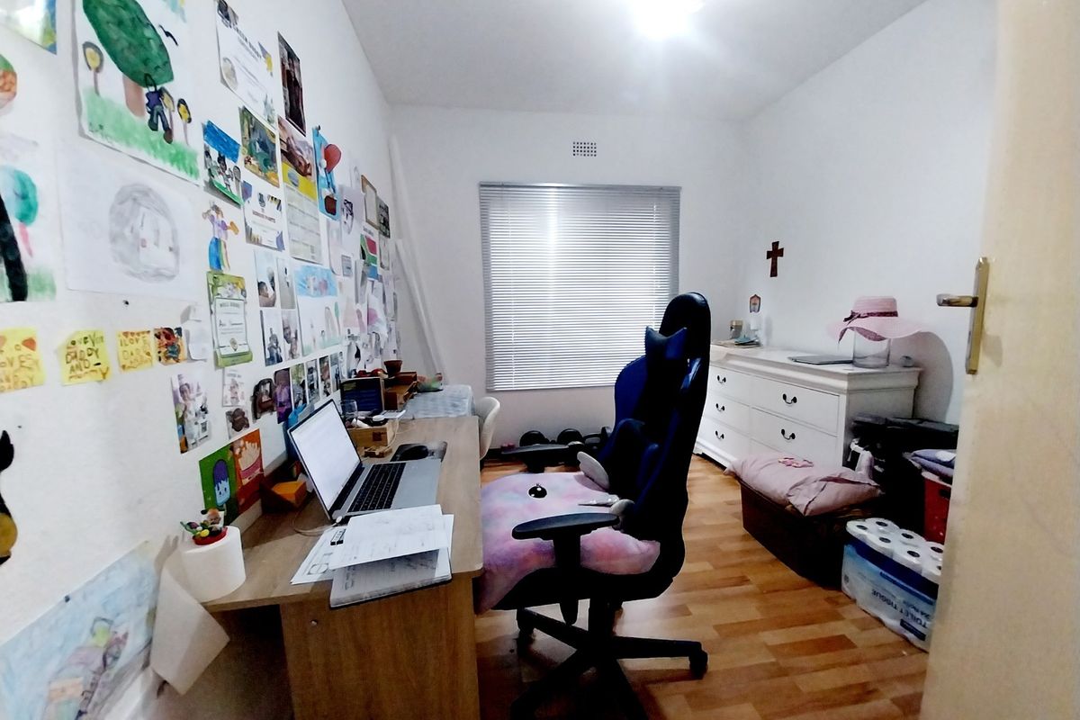 A functional bedroom featuring laminate flooring and venetian blinds, currently utilized as a home office and study space.