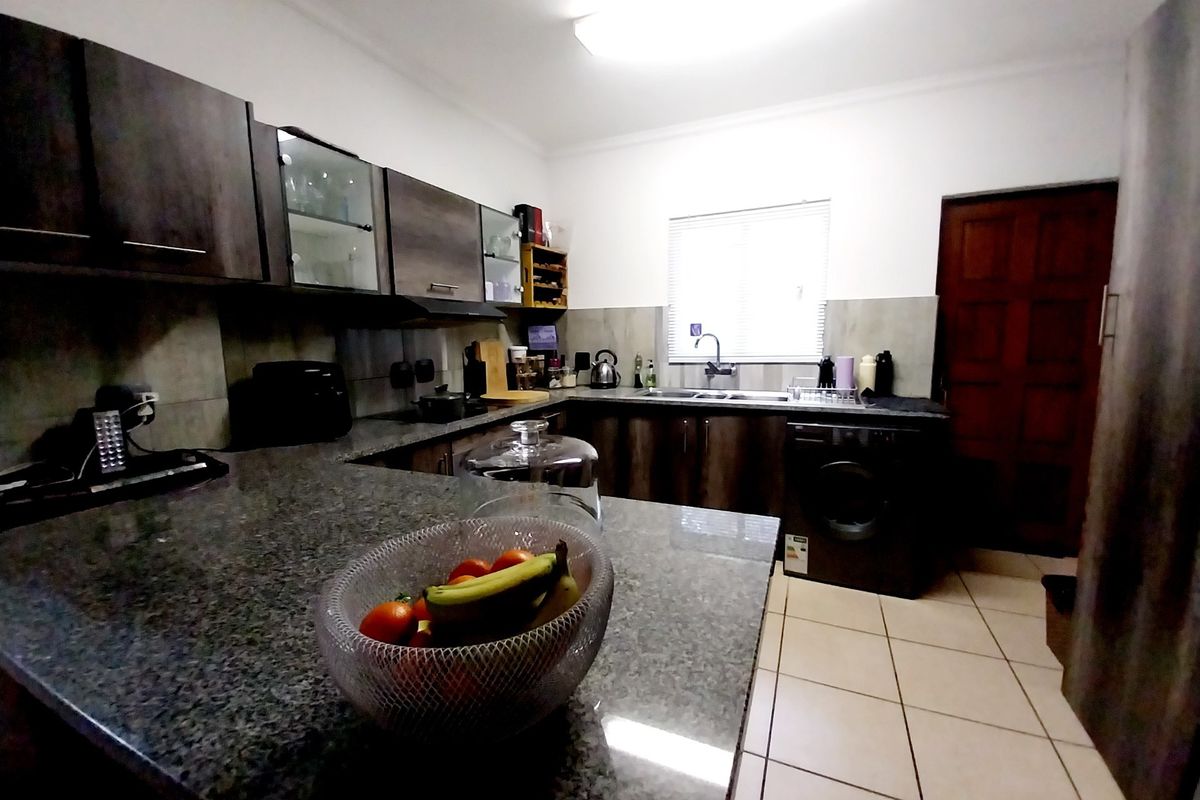 A functional kitchen featuring dark wood cabinetry, granite countertops, tiled flooring, and integrated appliances, offering a practical workspace with ample storage.