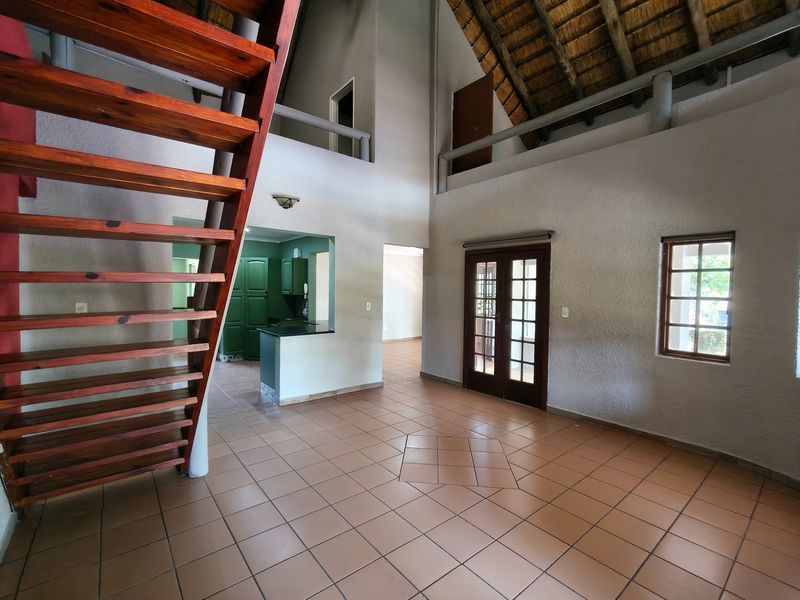 Spacious open-plan living area featuring a distinctive thatched roof, wooden staircase, mezzanine level, and direct access to the exterior through french doors.