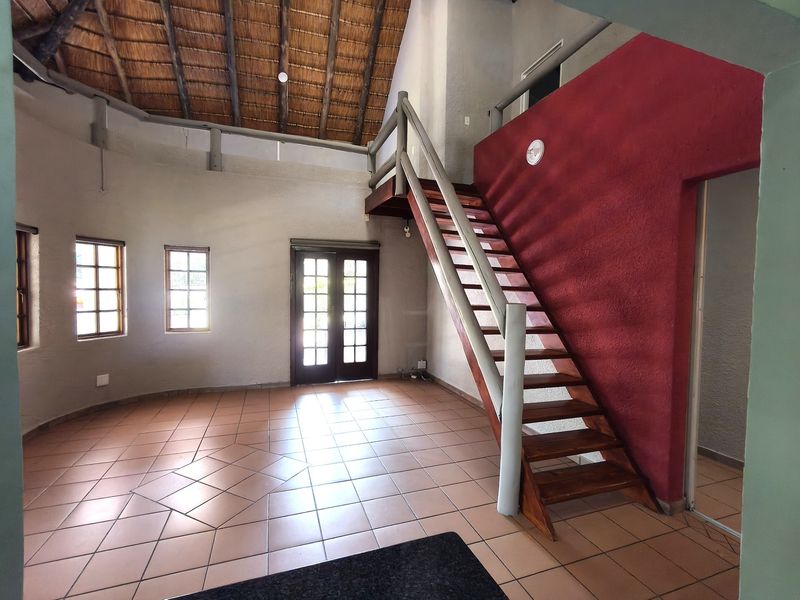 Spacious living area featuring a high thatched ceiling with exposed rafters, tiled flooring, and a timber staircase leading to an upper level.
