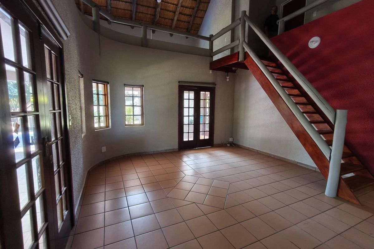 Spacious living area featuring a double-volume thatched ceiling, exposed timber staircase, terracotta tiled flooring, and multiple sets of french doors providing natural light.