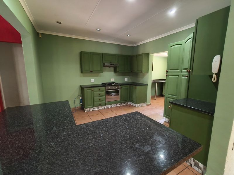 A spacious kitchen featuring green cabinetry, dark granite countertops, built-in oven and hob, and tiled flooring, offering a functional layout with ample storage.