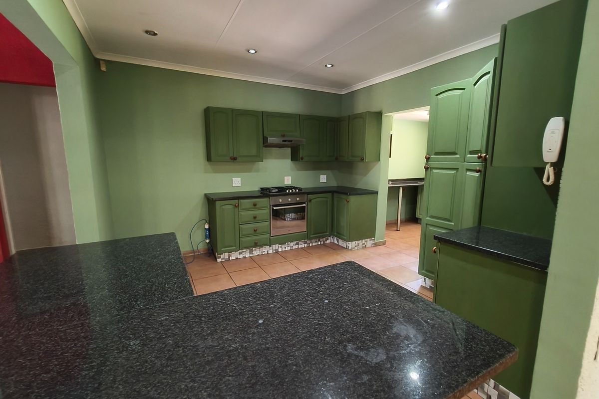 A spacious kitchen featuring green cabinetry, dark granite countertops, built-in oven and hob, and tiled flooring, offering a functional layout with ample storage.