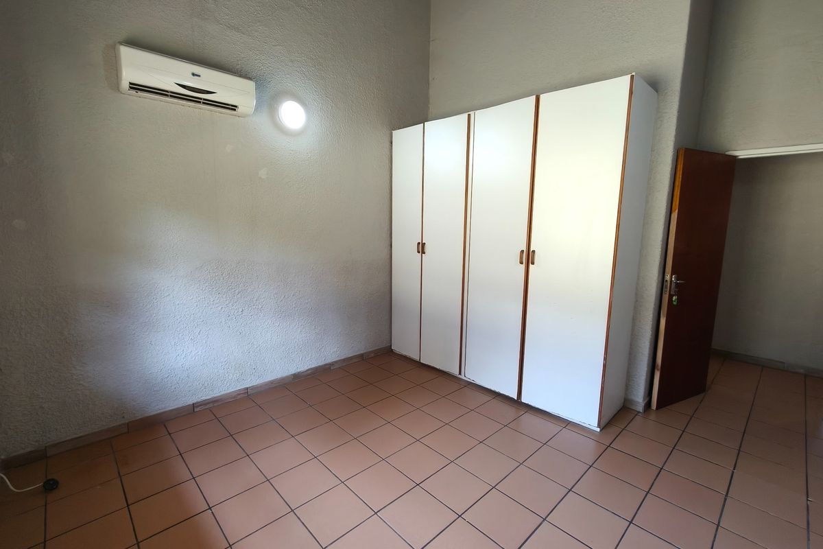 A spacious bedroom featuring tiled flooring, a built-in wardrobe, and a wall-mounted air conditioning unit.
