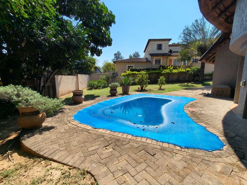 Outdoor pool area featuring a paved patio surround, a blue pool cover, and established garden landscaping with boundary walls.