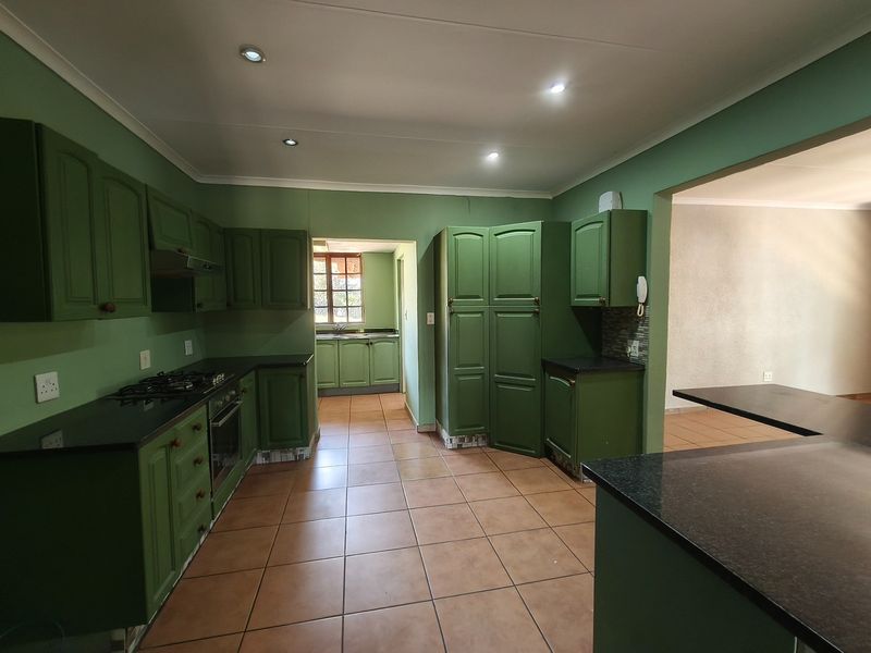 Spacious kitchen featuring green built-in cabinetry, granite countertops, gas hob, and tiled flooring, offering a functional layout with ample storage space.
