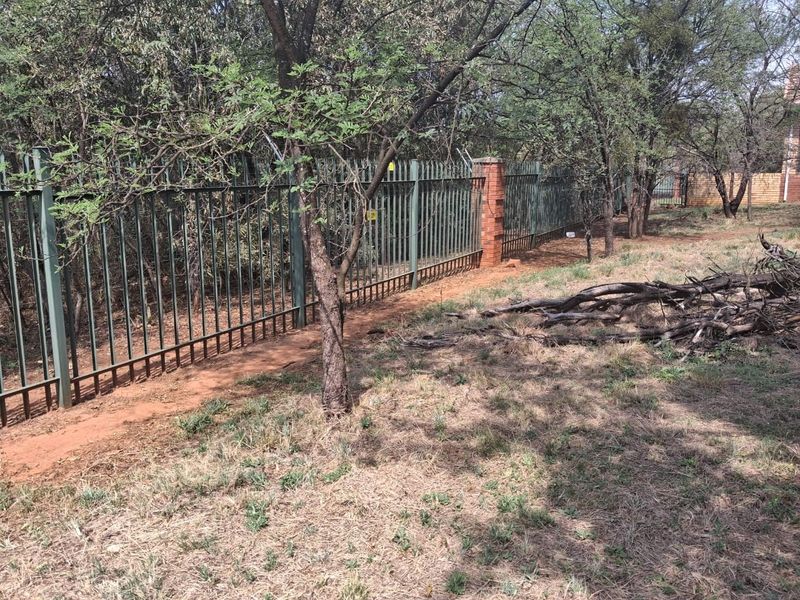 A view of the residential property boundary featuring steel palisade fencing with brick pillars and mature trees on the perimeter.
