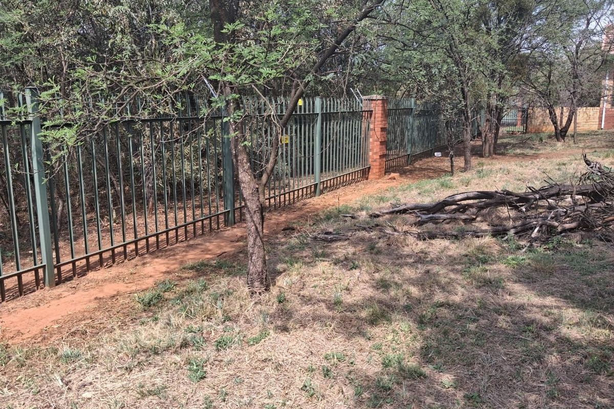 A view of the residential property boundary featuring steel palisade fencing with brick pillars and mature trees on the perimeter.