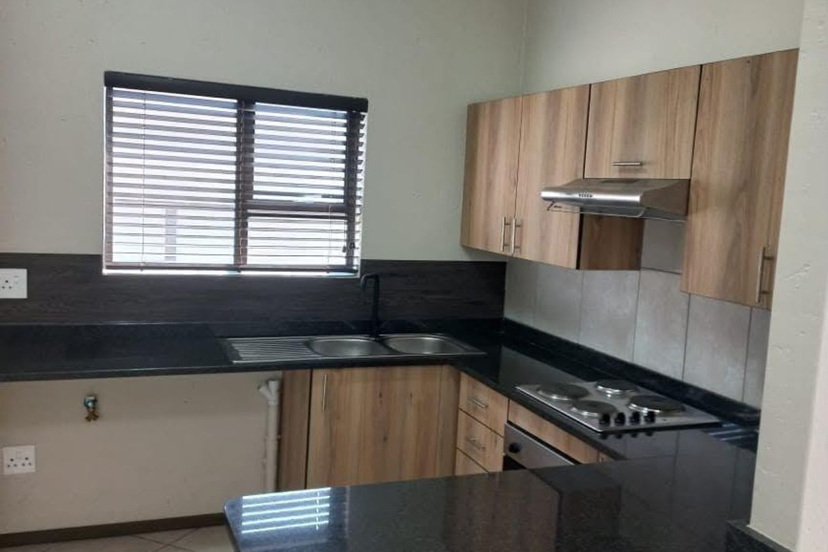 A clean, functional kitchen featuring wood-look cabinetry, dark granite countertops, built-in cooking appliances, and tiled flooring.
