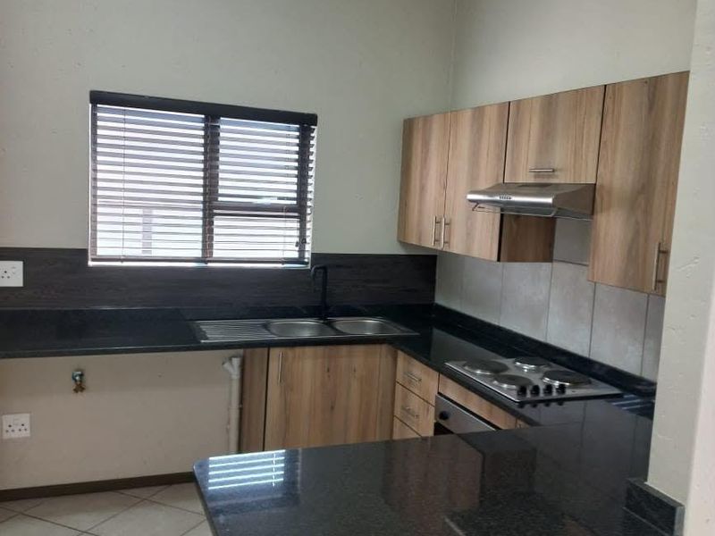 A clean, functional kitchen featuring wood-look cabinetry, dark granite countertops, built-in cooking appliances, and tiled flooring.