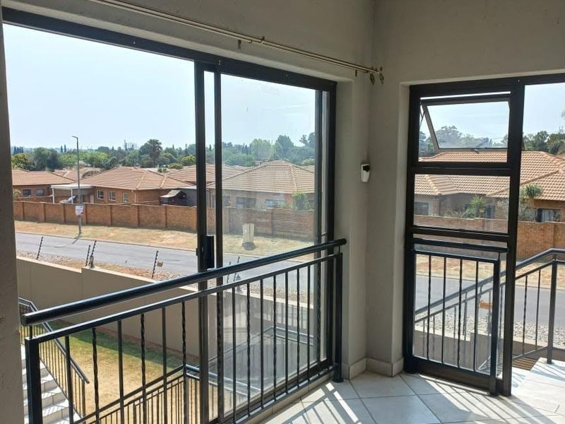 A covered balcony featuring tiled flooring, metal balustrades, and large sliding glass doors with views of the surrounding residential area.