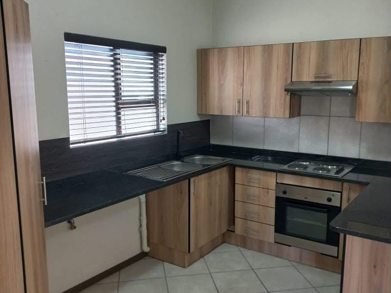 A functional kitchen featuring wood-look cabinetry, dark laminate countertops, built-in oven and hob, and tiled flooring with a window providing natural light.