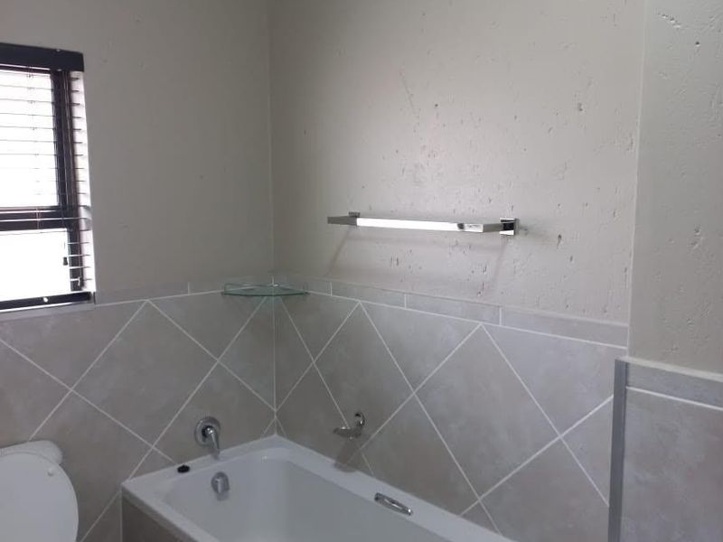 A functional bathroom featuring a bathtub, toilet, tiled splashbacks, and a chrome towel rail, presenting a clean but dated aesthetic.