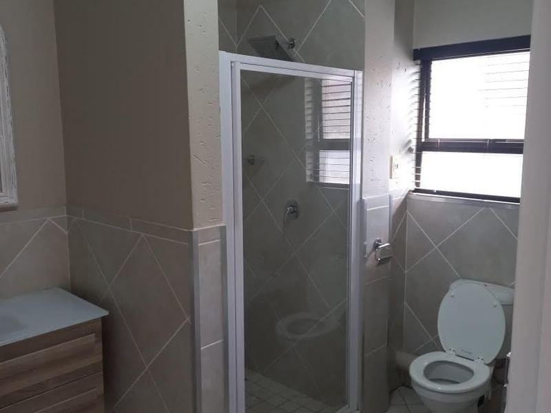 A functional bathroom featuring a shower enclosure, vanity cabinet, toilet, and neutral tiled finishes with natural light from the window.