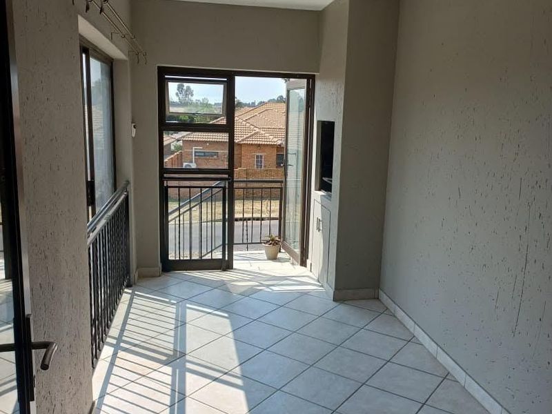 A covered balcony featuring tiled flooring, a built-in braai, and metal balustrades, offering an open-air space suitable for outdoor dining or relaxation.
