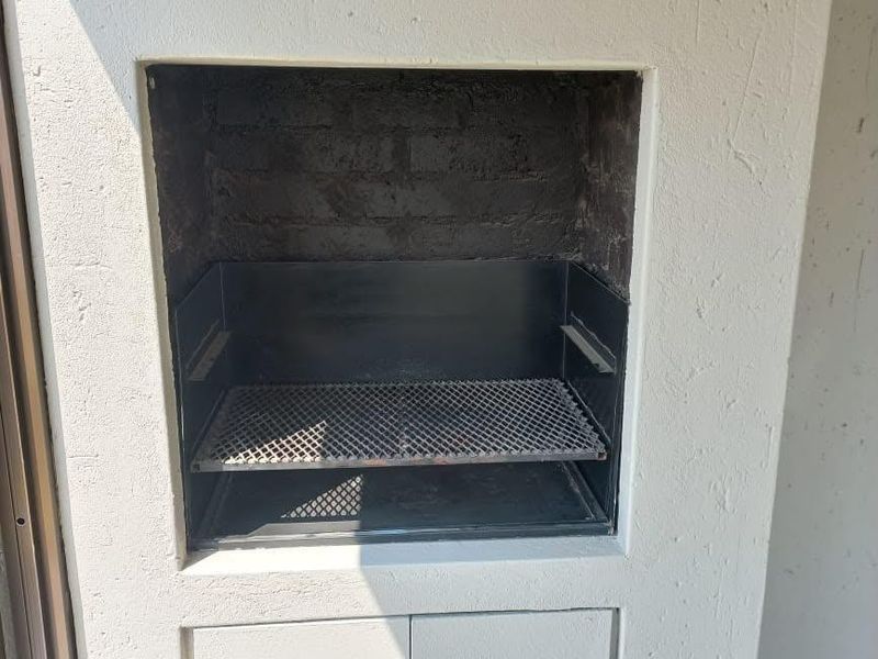 A built-in outdoor braai area featuring a metal grill and lower storage cabinetry, situated on a tiled patio or balcony.