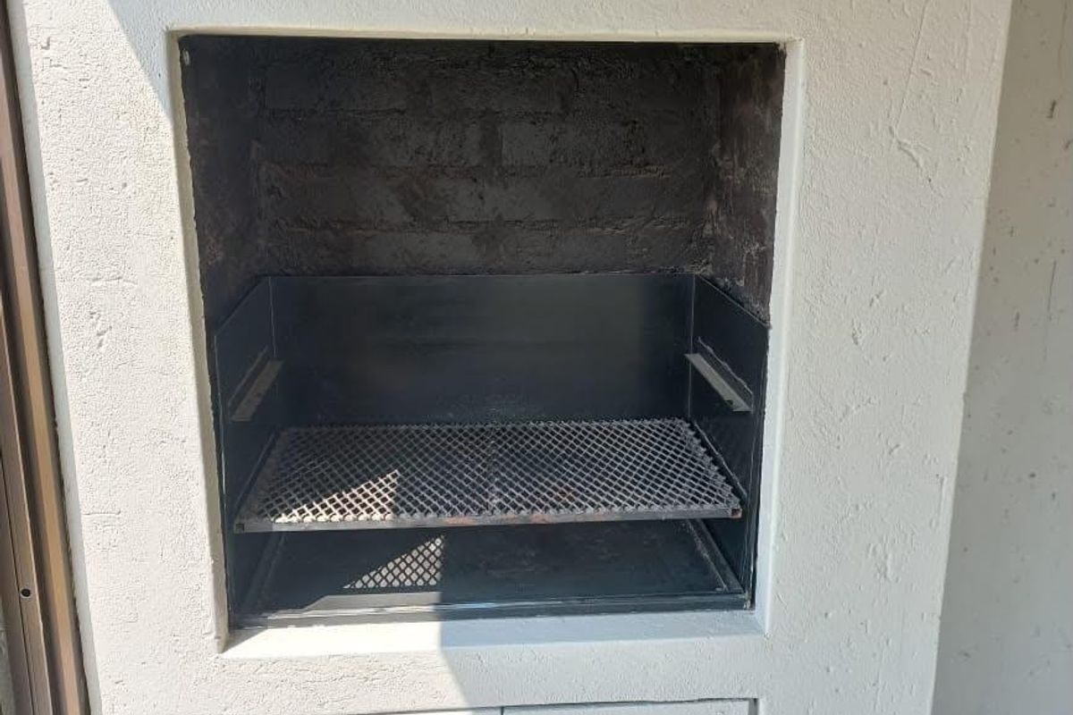 A built-in outdoor braai area featuring a metal grill and lower storage cabinetry, situated on a tiled patio or balcony.