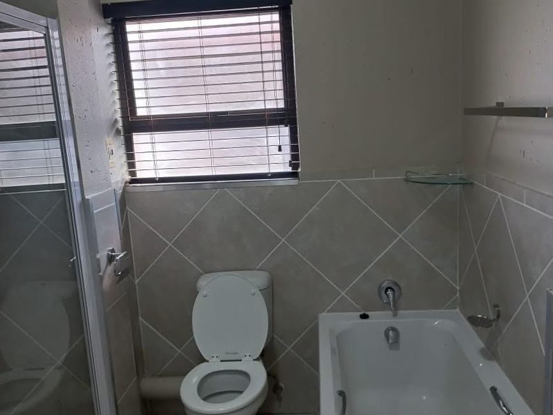 A functional bathroom featuring a bathtub, separate shower enclosure, toilet, and neutral tiled finishes with a window for natural light.