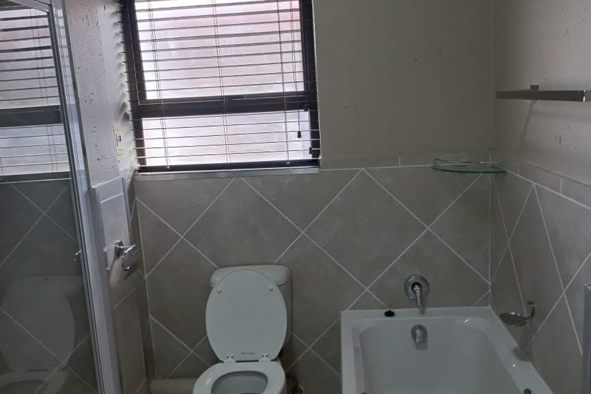 A functional bathroom featuring a bathtub, separate shower enclosure, toilet, and neutral tiled finishes with a window for natural light.