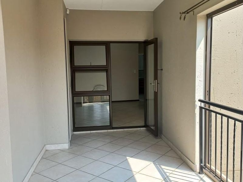 A clean, covered balcony featuring tiled flooring, a metal balustrade, and direct access to the interior living space through an aluminium glass door.