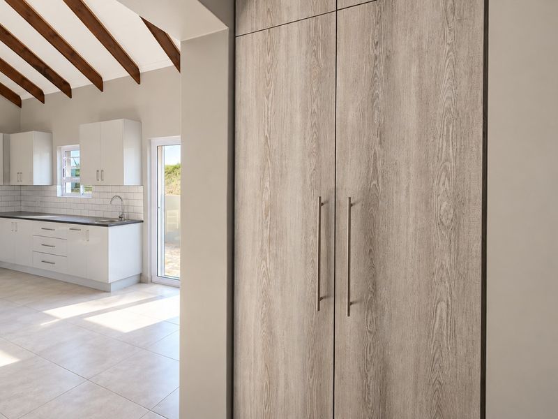 Modern kitchen featuring white cabinetry, subway tile backsplash, and exposed timber ceiling beams, leading to an outdoor area with tiled flooring throughout.