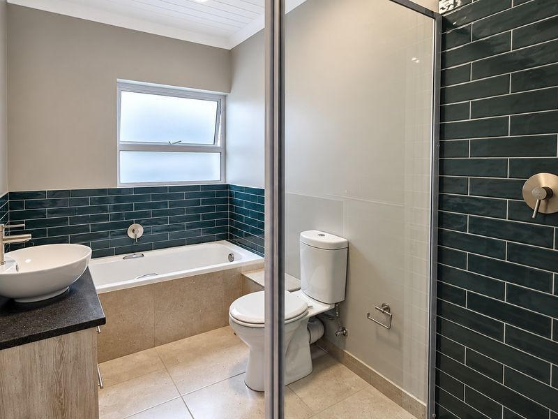 Modern bathroom featuring a glass-enclosed shower, built-in bathtub, vessel sink vanity, and stylish dark green subway tile accents.
