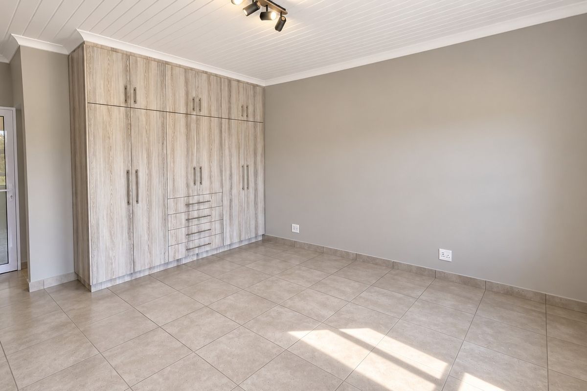 A bright, empty bedroom featuring modern wood-look built-in cupboards, neutral tiled flooring, and a clean tongue and groove ceiling.