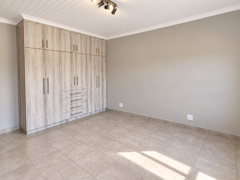 A bright, empty bedroom featuring modern wood-look built-in cupboards, neutral tiled flooring, and a clean tongue and groove ceiling.