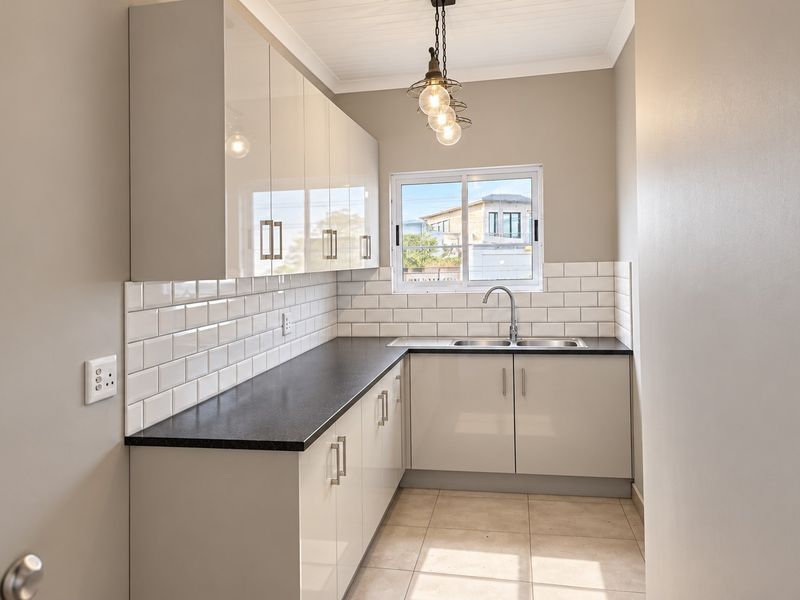 A clean, modern scullery featuring gloss cabinetry, subway tile backsplash, dark laminate countertops, and a stainless steel double sink with a mixer tap.