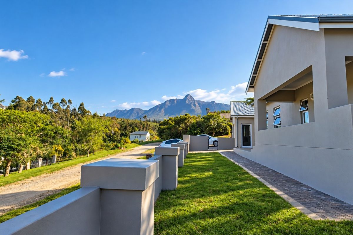 A well-maintained rear exterior view of the property featuring a paved walkway, manicured lawn, boundary wall, and scenic mountain views.