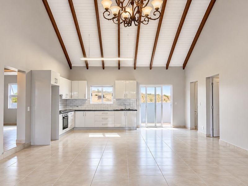 Spacious open-plan kitchen and living area featuring vaulted ceilings with exposed timber beams, tiled flooring, and direct access to an outdoor patio.