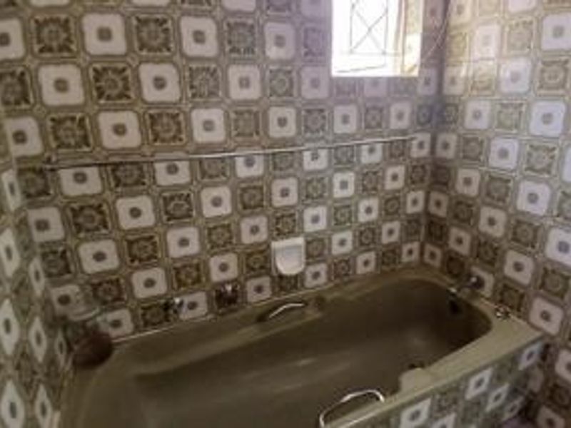 A dated bathroom featuring a built-in bathtub with vintage patterned wall tiles and chrome fixtures, offering potential for a modern renovation.