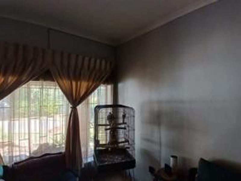 A living room area featuring large windows with security bars and decorative curtain rails, providing natural light to the space.