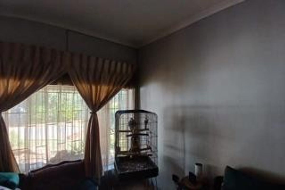 A living room area featuring large windows with security bars and decorative curtain rails, providing natural light to the space.