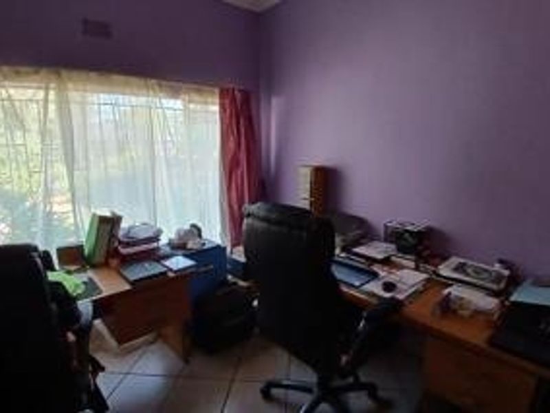 A functional home office space featuring tiled flooring and a large window with security bars, providing natural light.