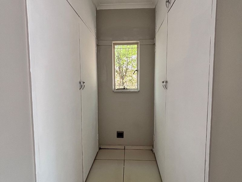 A narrow hallway featuring extensive built-in storage cupboards, tiled flooring, and a window with security bars.